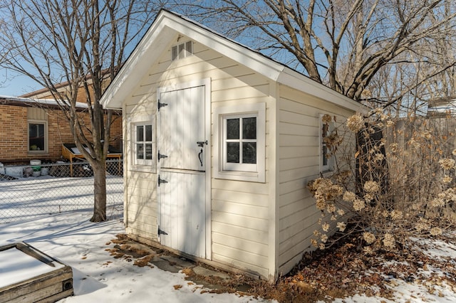 snow covered structure with fence and an outbuilding