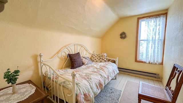 bedroom with vaulted ceiling, baseboard heating, a textured wall, and hardwood / wood-style floors