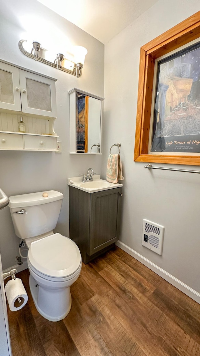 half bathroom featuring vanity, toilet, wood finished floors, and baseboards