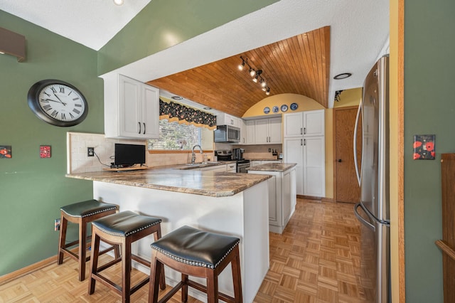 kitchen with baseboards, lofted ceiling, a peninsula, a sink, and appliances with stainless steel finishes