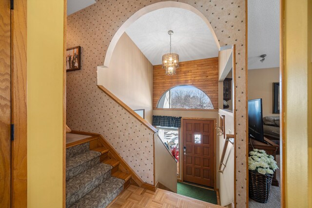 entrance foyer with stairway, arched walkways, a chandelier, and wallpapered walls