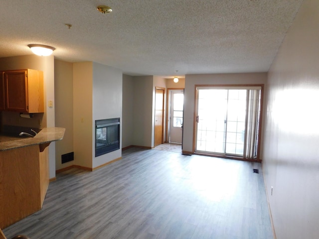 unfurnished living room featuring visible vents, light wood-style flooring, a multi sided fireplace, a textured ceiling, and baseboards