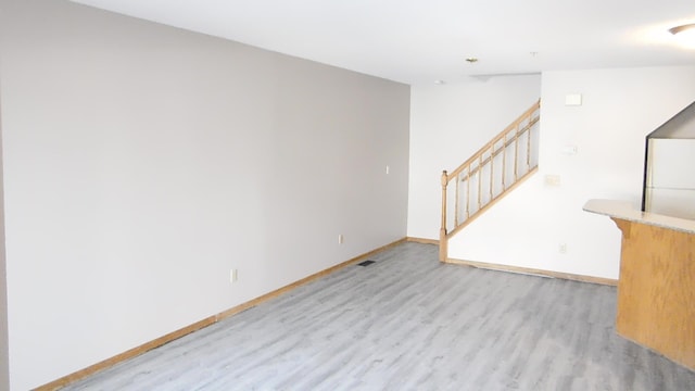 empty room with stairs, light wood-style flooring, and baseboards