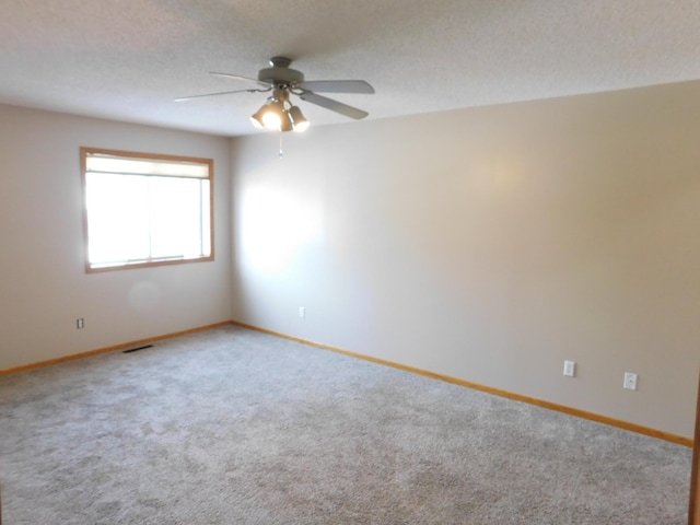 unfurnished room with a textured ceiling, carpet flooring, visible vents, and baseboards