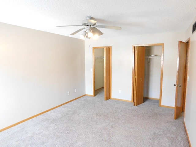 unfurnished bedroom with light carpet, a textured ceiling, baseboards, and multiple closets