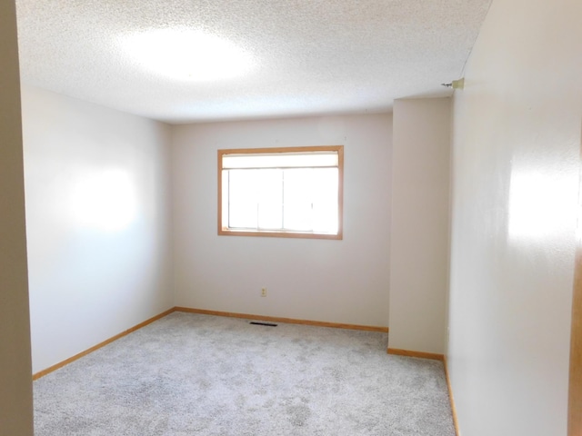 carpeted empty room featuring visible vents, a textured ceiling, and baseboards