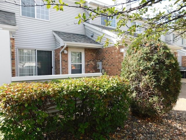 view of side of property with a shingled roof and brick siding