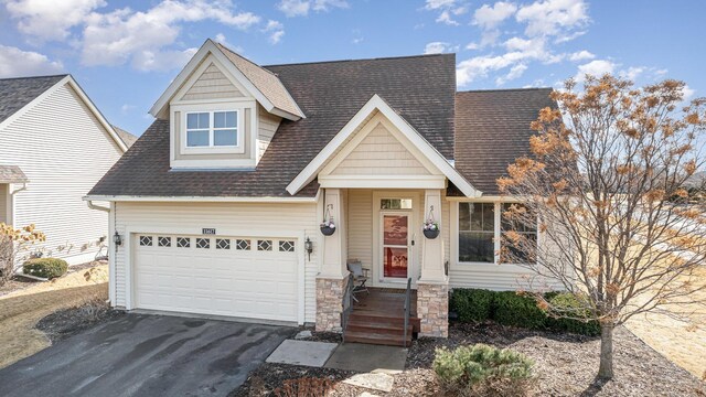 view of front facade with a garage, stone siding, roof with shingles, and driveway