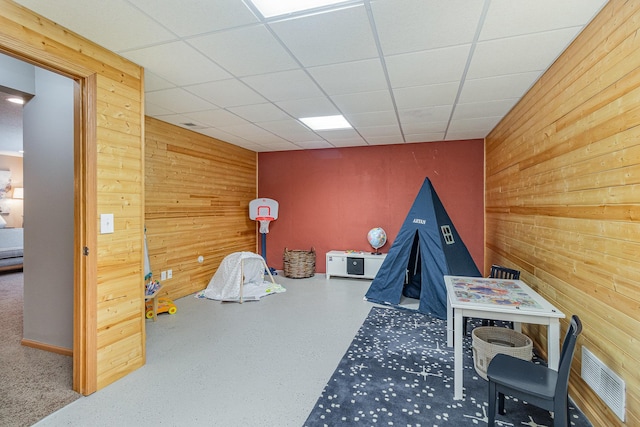 rec room with a paneled ceiling, visible vents, and wood walls