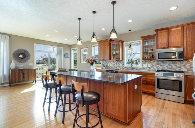 kitchen with a center island, light wood-style flooring, brown cabinetry, stainless steel appliances, and a sink