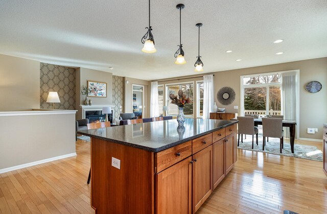 kitchen with a kitchen island, decorative light fixtures, light wood-type flooring, a fireplace, and a textured ceiling