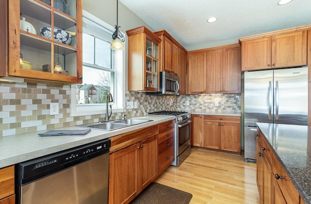 kitchen featuring pendant lighting, light wood-style flooring, brown cabinetry, stainless steel appliances, and a sink