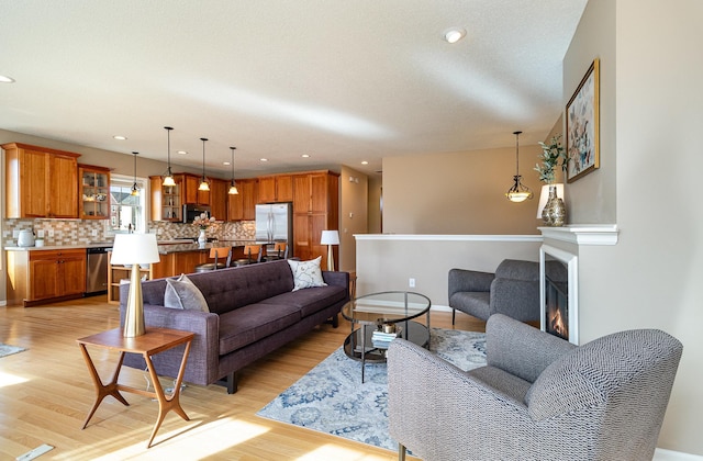 living area with recessed lighting, light wood-style floors, baseboards, and a lit fireplace