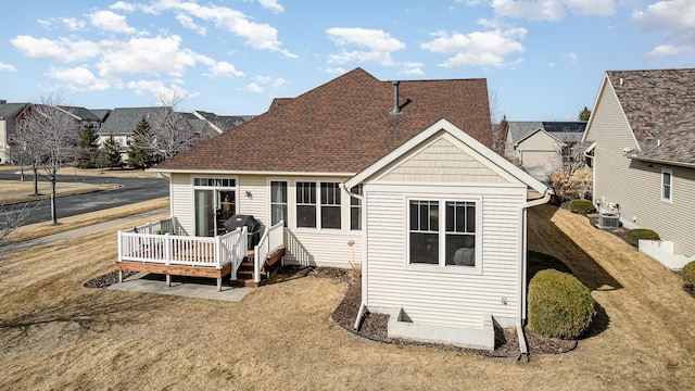 rear view of house featuring a shingled roof, a yard, and a wooden deck