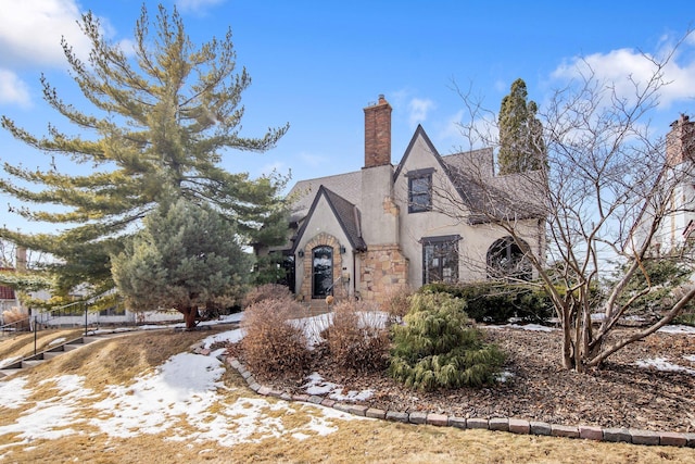 tudor house with a chimney, stone siding, and stucco siding