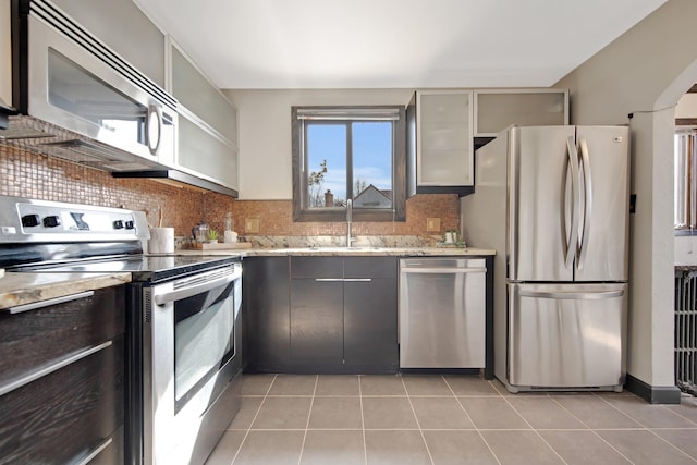 kitchen featuring tasteful backsplash, light tile patterned flooring, stainless steel appliances, and a sink