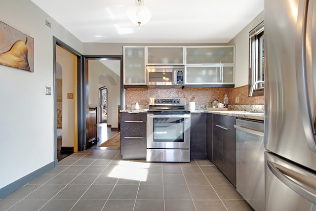 kitchen with arched walkways, backsplash, appliances with stainless steel finishes, and dark tile patterned floors