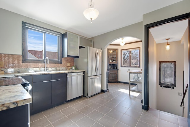 kitchen with a sink, stainless steel appliances, arched walkways, and backsplash