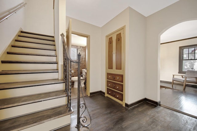 stairs featuring arched walkways, baseboards, and wood finished floors