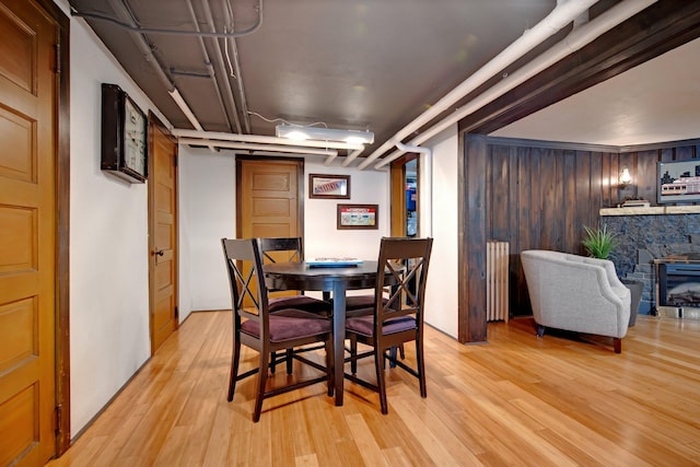 dining room featuring radiator, wooden walls, light wood-style floors, and a fireplace