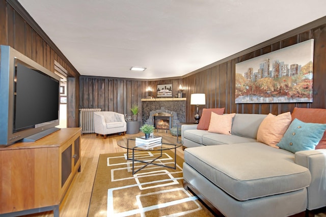 living room featuring a stone fireplace, light wood-style flooring, radiator, and wooden walls