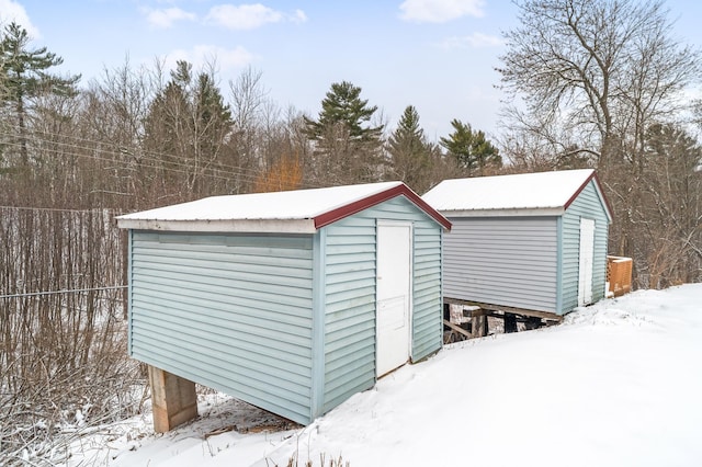 snow covered structure with a storage shed, fence, and an outdoor structure