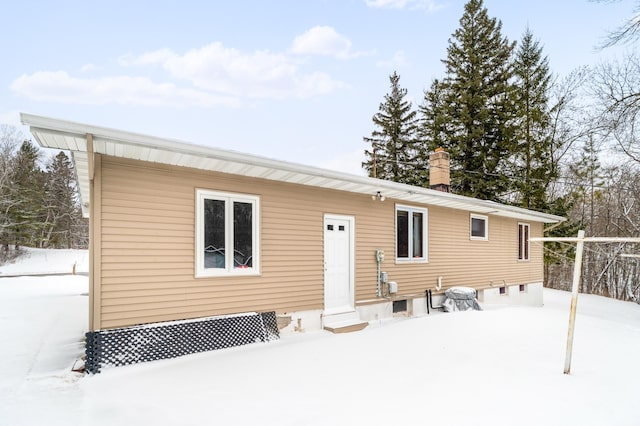 snow covered rear of property featuring entry steps and a chimney