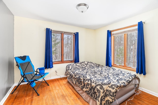 bedroom with multiple windows, baseboards, and wood finished floors