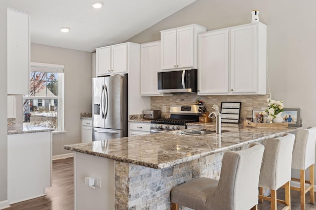 kitchen with a sink, light stone countertops, appliances with stainless steel finishes, and a peninsula