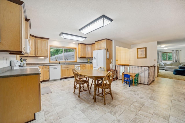 kitchen with a sink, white appliances, dark countertops, and a wealth of natural light