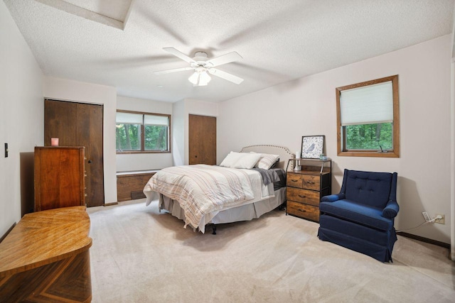 bedroom with two closets, a ceiling fan, a textured ceiling, baseboards, and light colored carpet