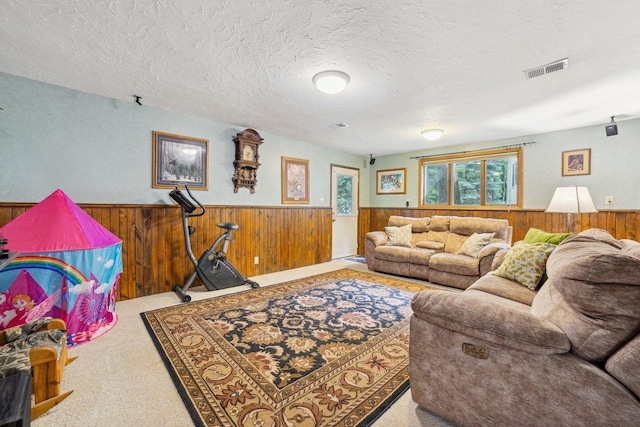 living area featuring wooden walls, carpet, visible vents, wainscoting, and a textured ceiling