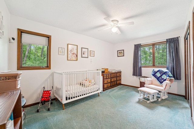 carpeted bedroom featuring a nursery area, baseboards, a textured ceiling, and ceiling fan