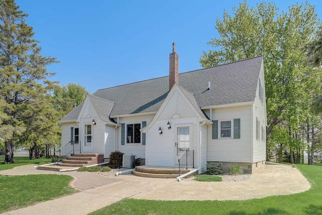 view of front facade with a front yard, a chimney, central AC unit, and roof with shingles