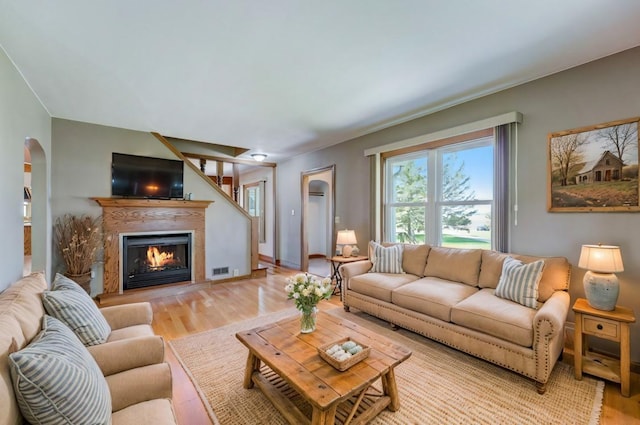 living area with arched walkways, visible vents, light wood-style floors, a warm lit fireplace, and baseboards