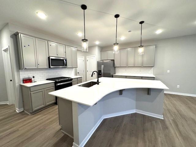 kitchen with gray cabinets, appliances with stainless steel finishes, dark wood-type flooring, a sink, and an island with sink