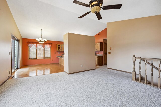 spare room with ceiling fan with notable chandelier, lofted ceiling, light colored carpet, and baseboards