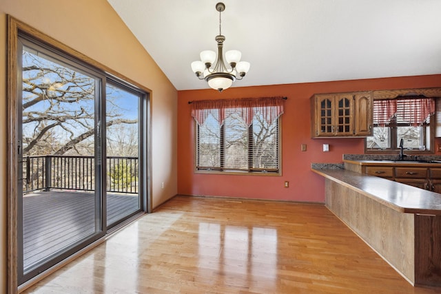 unfurnished dining area with a sink, light wood-type flooring, a chandelier, and vaulted ceiling