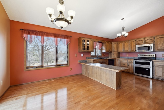 kitchen with glass insert cabinets, a chandelier, a peninsula, brown cabinetry, and stainless steel appliances