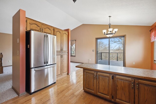 kitchen with a chandelier, decorative light fixtures, vaulted ceiling, brown cabinets, and freestanding refrigerator