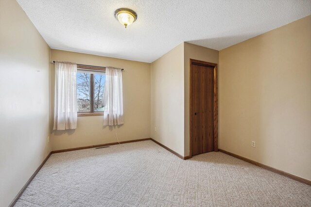 spare room featuring a textured ceiling, carpet, and baseboards