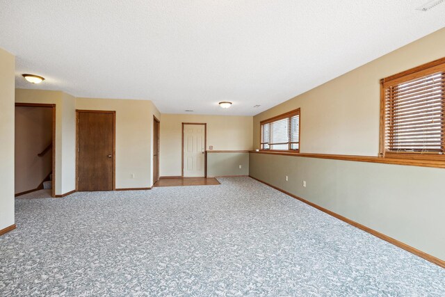 carpeted empty room with stairway, a textured ceiling, and baseboards