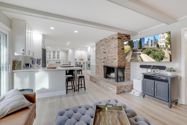 living room with light wood finished floors, beam ceiling, recessed lighting, a fireplace, and plenty of natural light