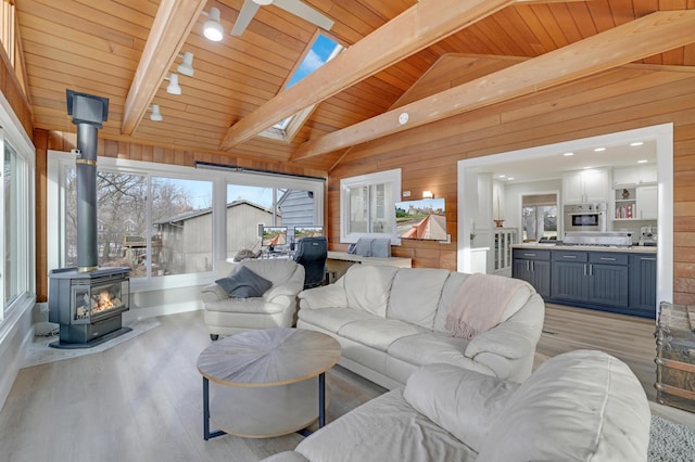 living area featuring light wood finished floors, wooden walls, a healthy amount of sunlight, vaulted ceiling with skylight, and a wood stove