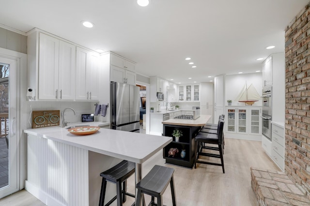 kitchen with a breakfast bar, white cabinets, stainless steel appliances, and light countertops