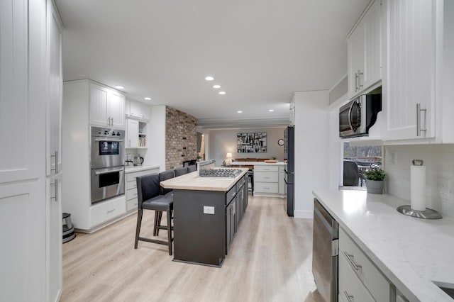 kitchen featuring light wood-type flooring, a kitchen island, tasteful backsplash, stainless steel appliances, and white cabinets