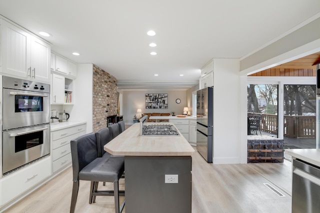 kitchen with a kitchen island, light wood-type flooring, appliances with stainless steel finishes, a kitchen breakfast bar, and white cabinets