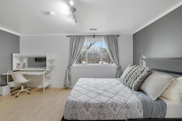 bedroom with crown molding, wood finished floors, visible vents, and track lighting