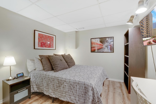 bedroom featuring a drop ceiling, light wood-style flooring, baseboards, and visible vents