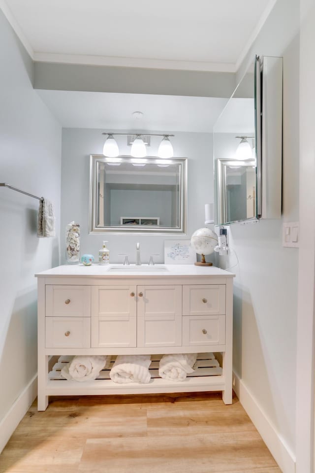 bathroom featuring baseboards, wood finished floors, vanity, and crown molding